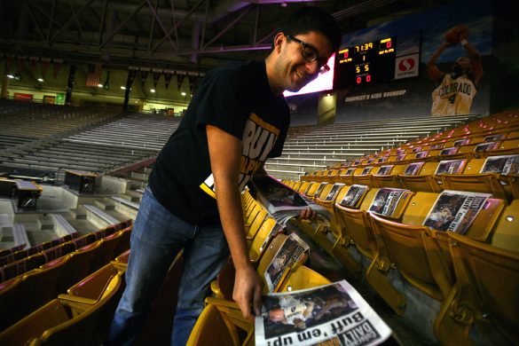 Ian Solow-Niederman, executive director of the C-Unit, lays newspaper on every seat in the first 15 rows of the east side of the Coors Events Center for students to use during the College GameDay broadcast. (Kai Casey/CU Independent)