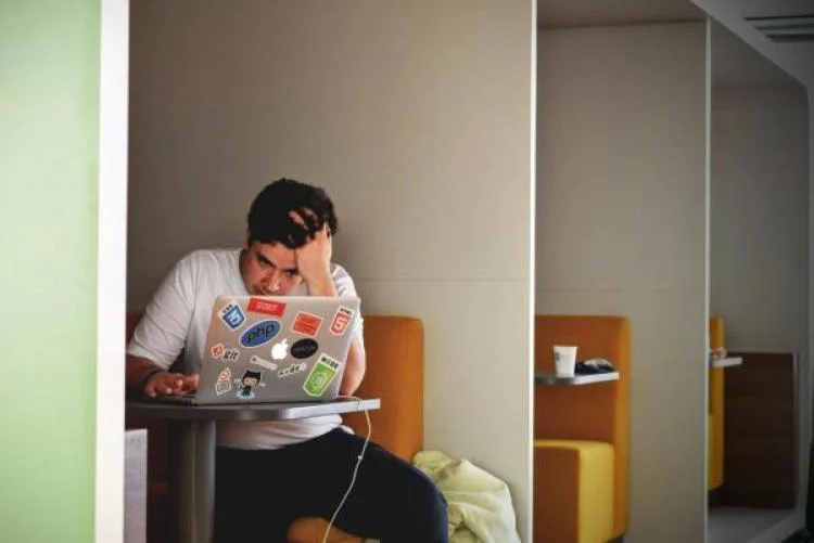 A student looking at a laptop with his hand running through his hair, a stressed expression on his face.