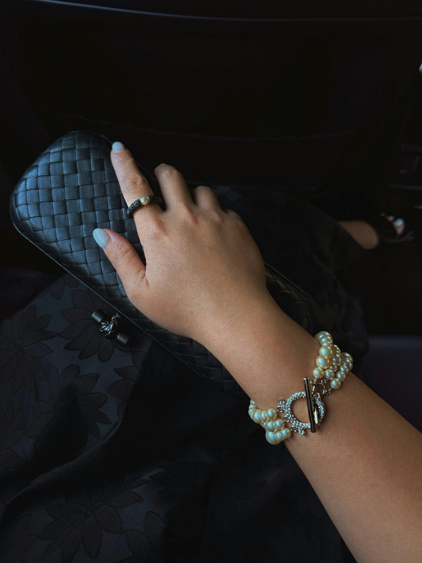 Woman's hand with pearl bracelet and ring on handbag