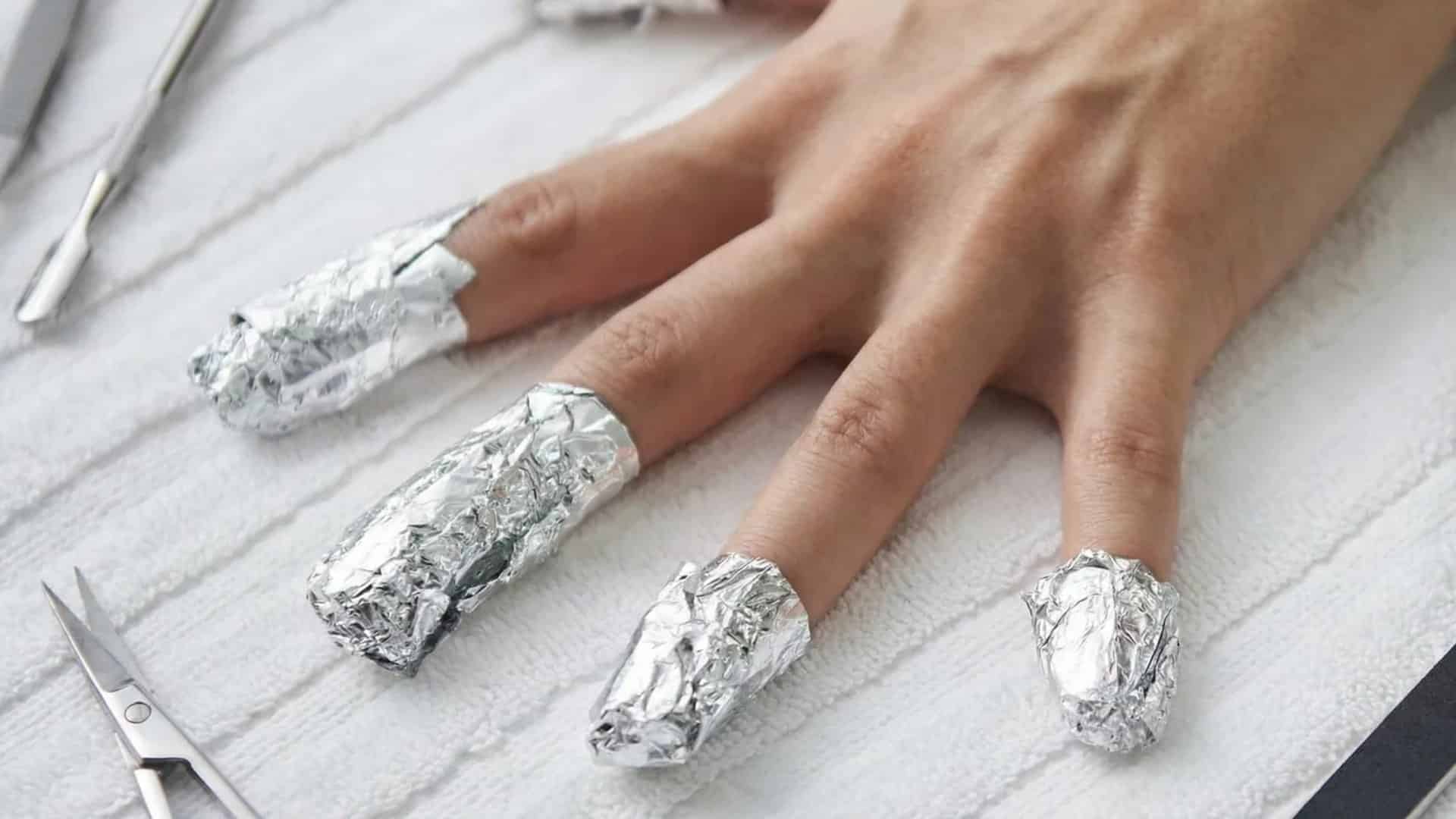 Hand with nails wrapped in foil on a towel, with manicure tools nearby.