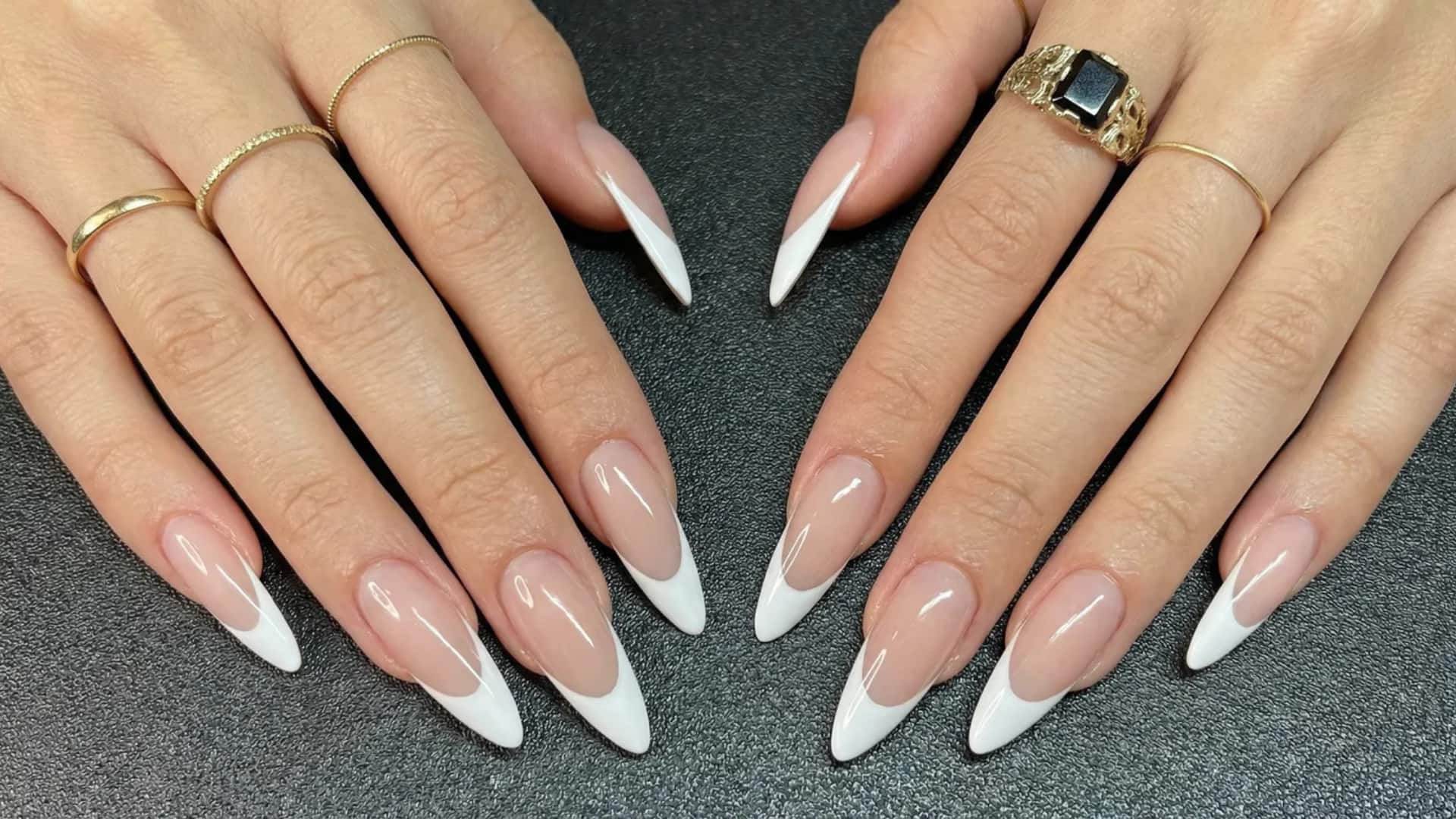Hands with long nude acrylic nails and white French tips on a dark surface.