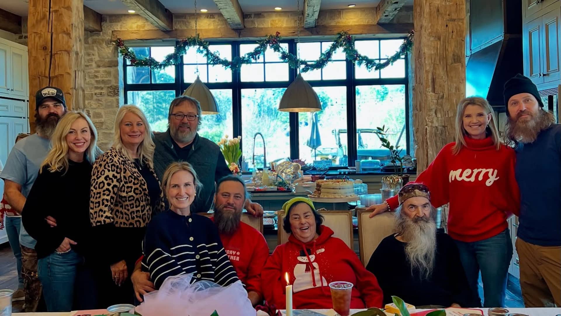 Phil Robertson seated with family during a holiday gathering at home, surrounded by relatives in a cozy kitchen setting