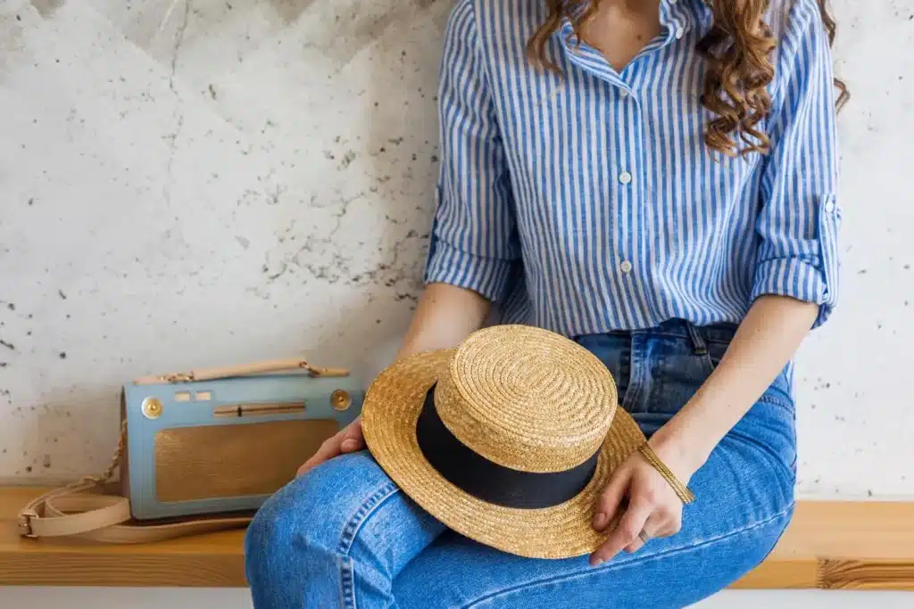 Woman in striped blue shirt holding straw hat sitting on wooden bench