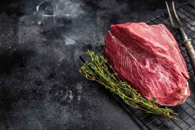 Raw beef steak with fresh thyme on metal rack against dark textured background