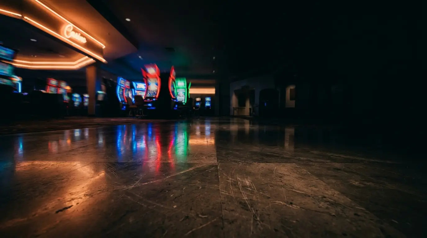 Dimly lit casino floor with colorful slot machines reflecting on polished tiles