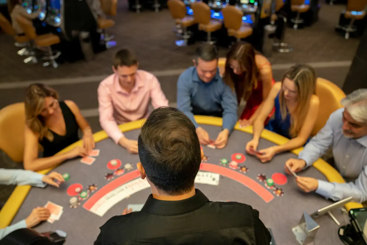 Dealer and players at a poker table in a casino setting with colorful chips