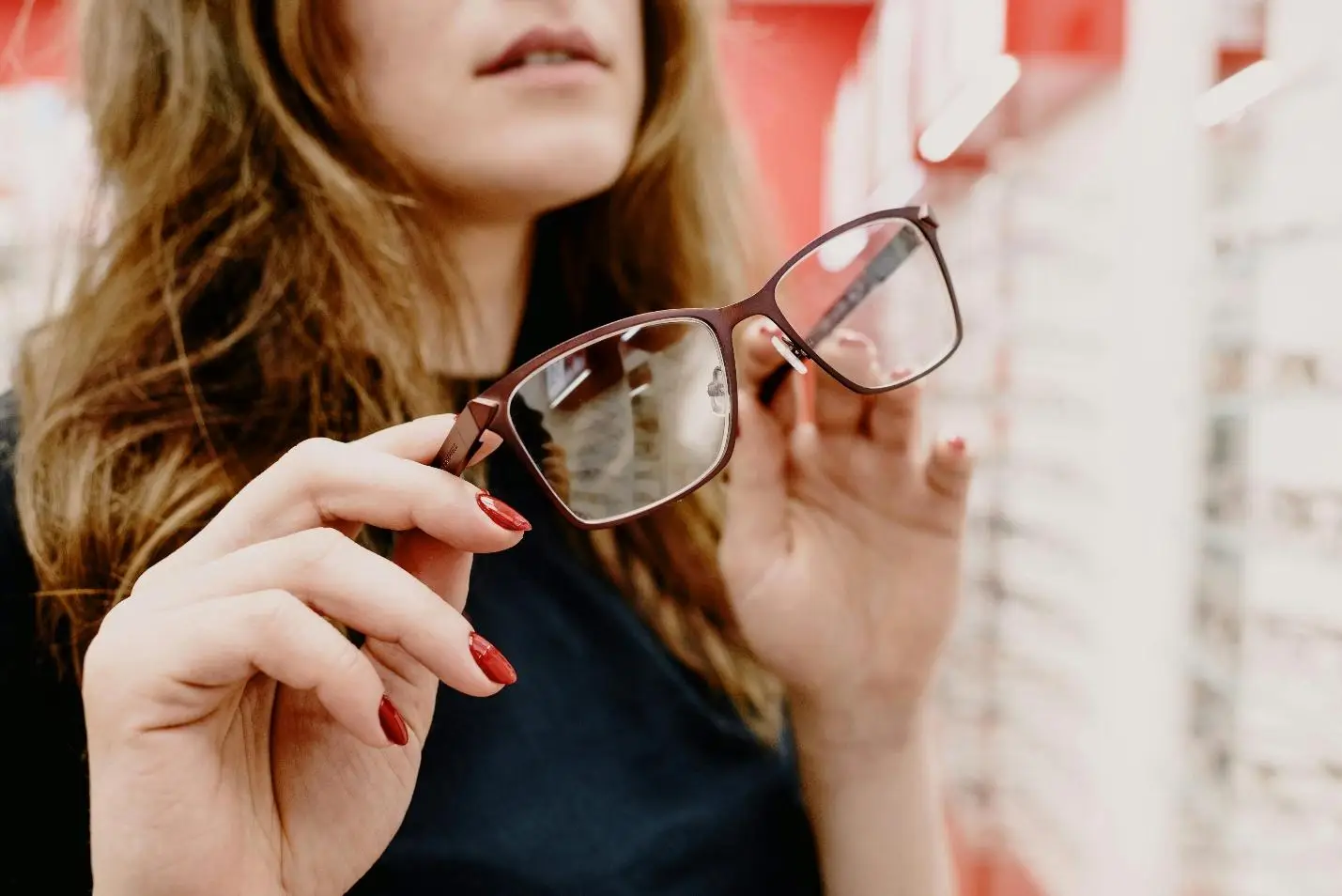 Woman holding glasses in bright optical store with red background