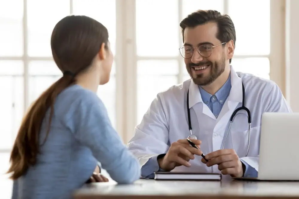 Doctor consulting patient in bright office with large windows and a laptop on the desk