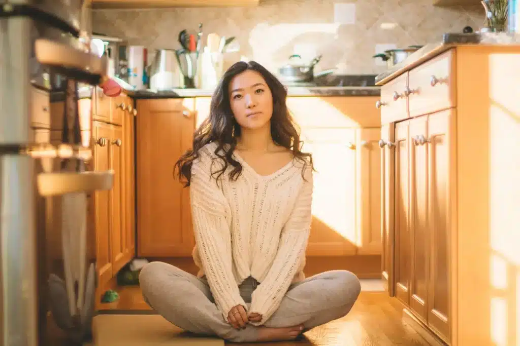 Woman sitting cross-legged on wooden kitchen floor in natural sunlight