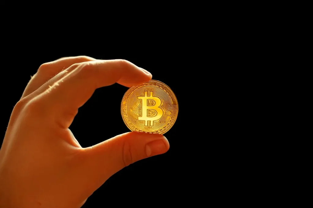 Hand holding a gold Bitcoin coin against a black background