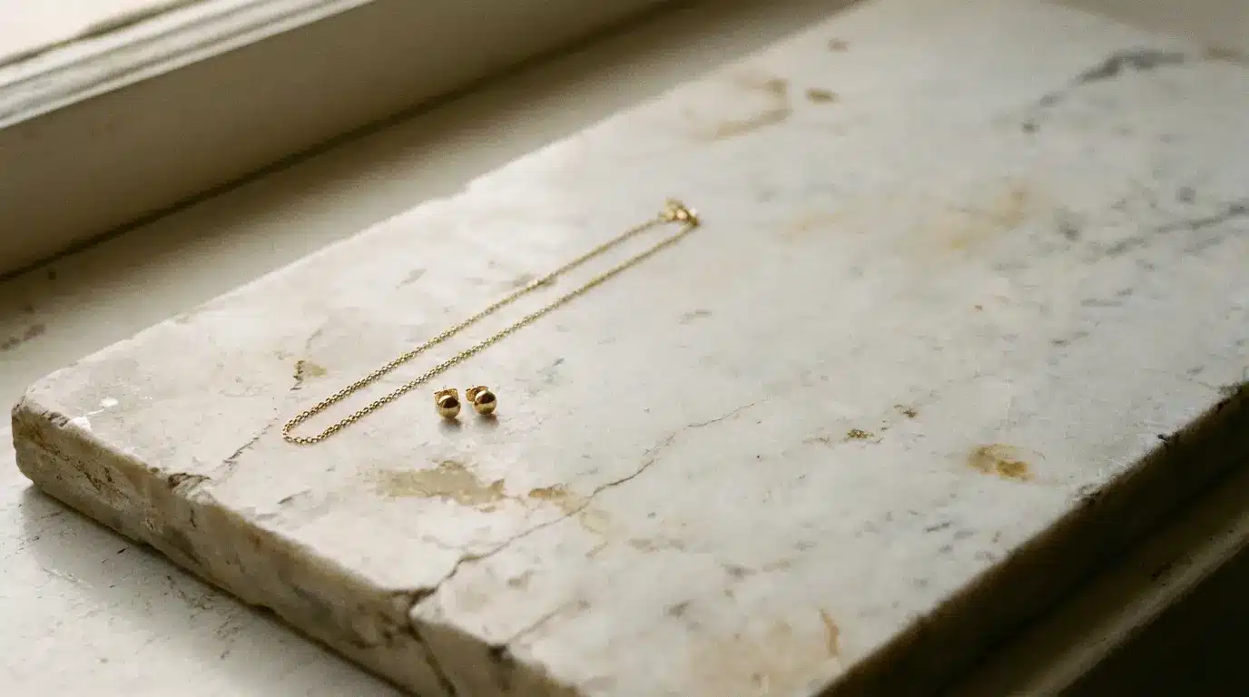 Gold chain necklace and earrings on a textured marble surface in soft natural light