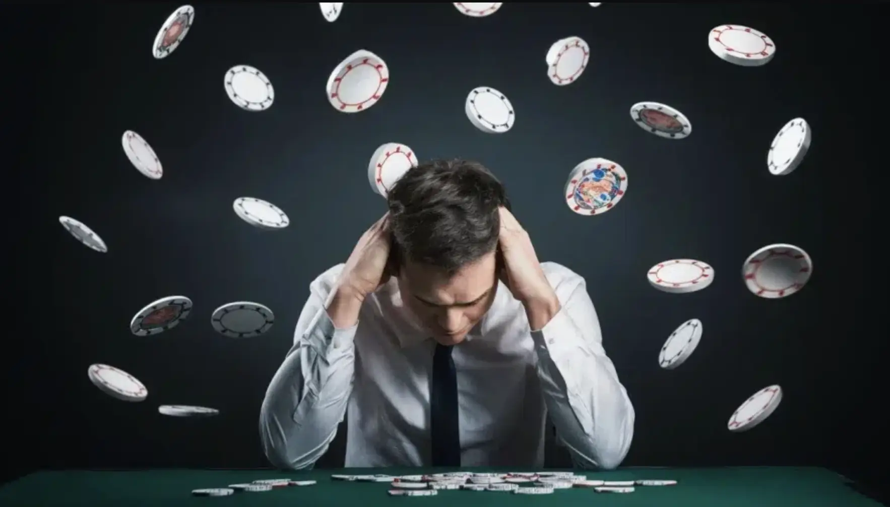 Man in white shirt holding head surrounded by flying poker chips in dark setting
