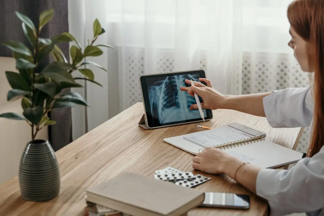Doctor analyzing chest X-ray on tablet in sunlit office with notepad and plant nearby