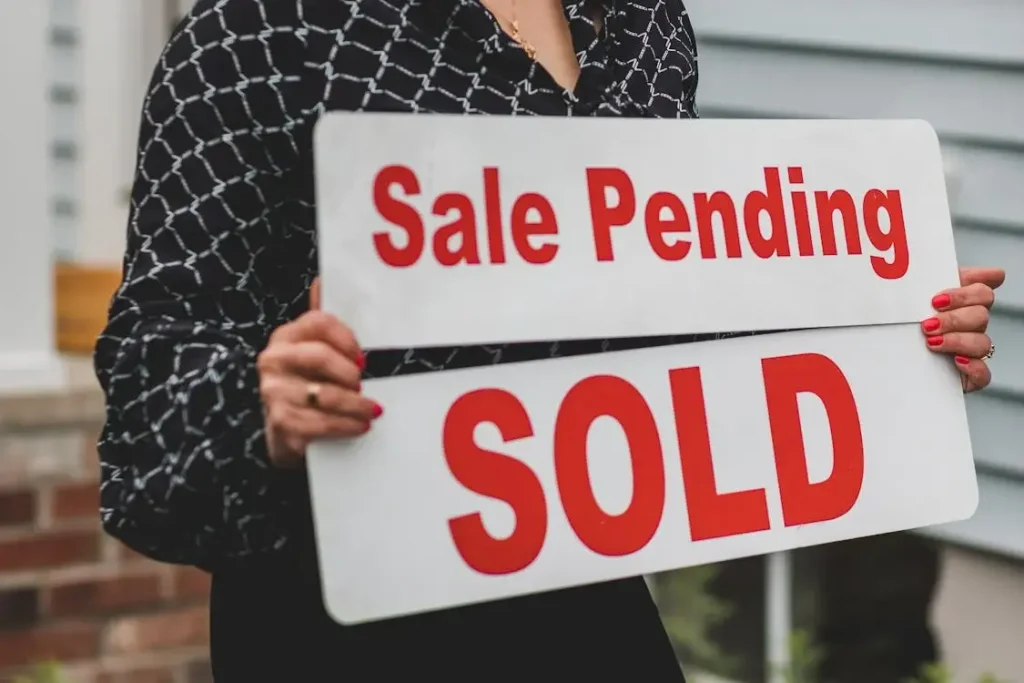 Person holding sale pending and sold signs in front of a house exterior