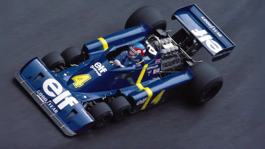 Blue Formula One car with yellow accents racing on track, driver in helmet and racing suit