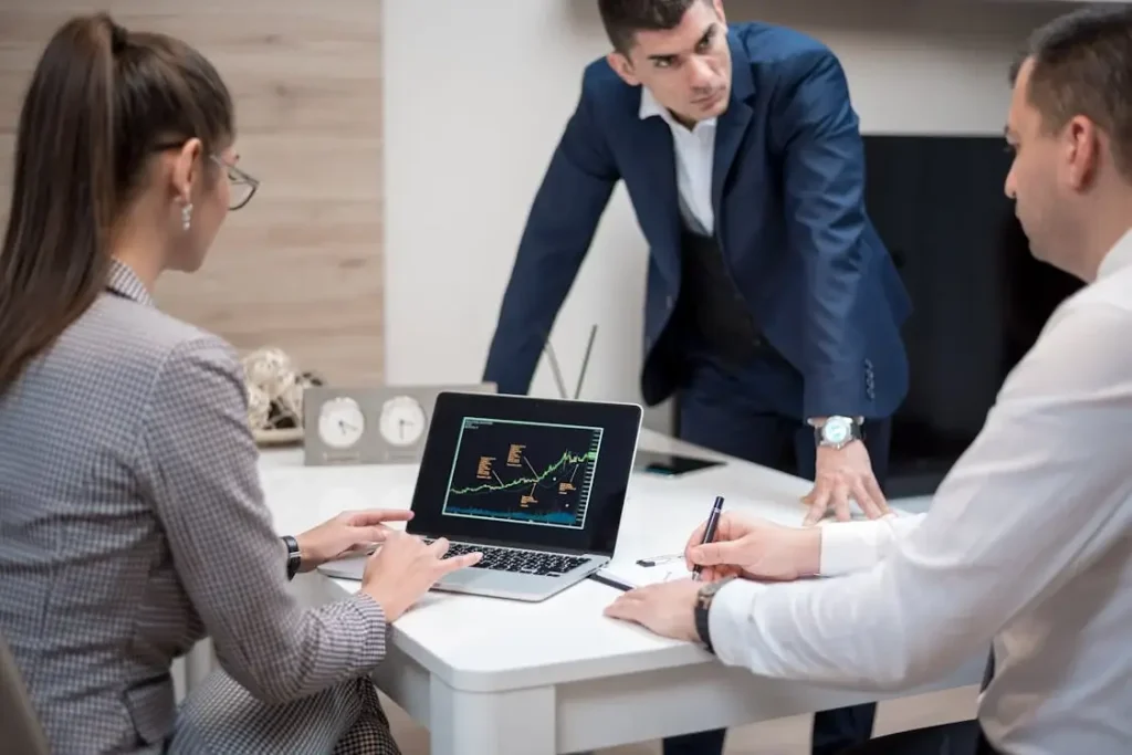 Business meeting with professionals reviewing stock market data on laptop screen in office setting