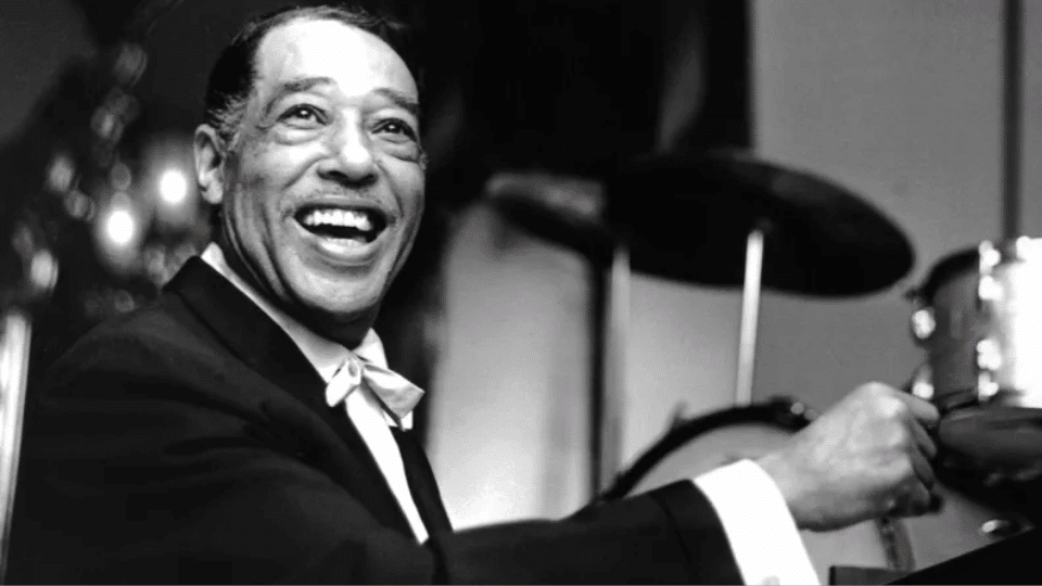 Duke Ellington in a suit playing drums.
