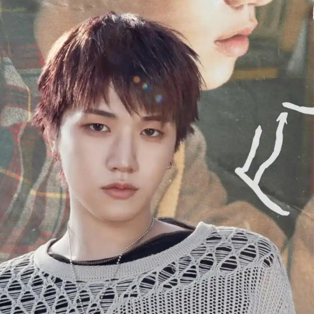 BOYNEXTDOOR member with short brown hair wearing a gray mesh sweater and necklace, looking at the camera.