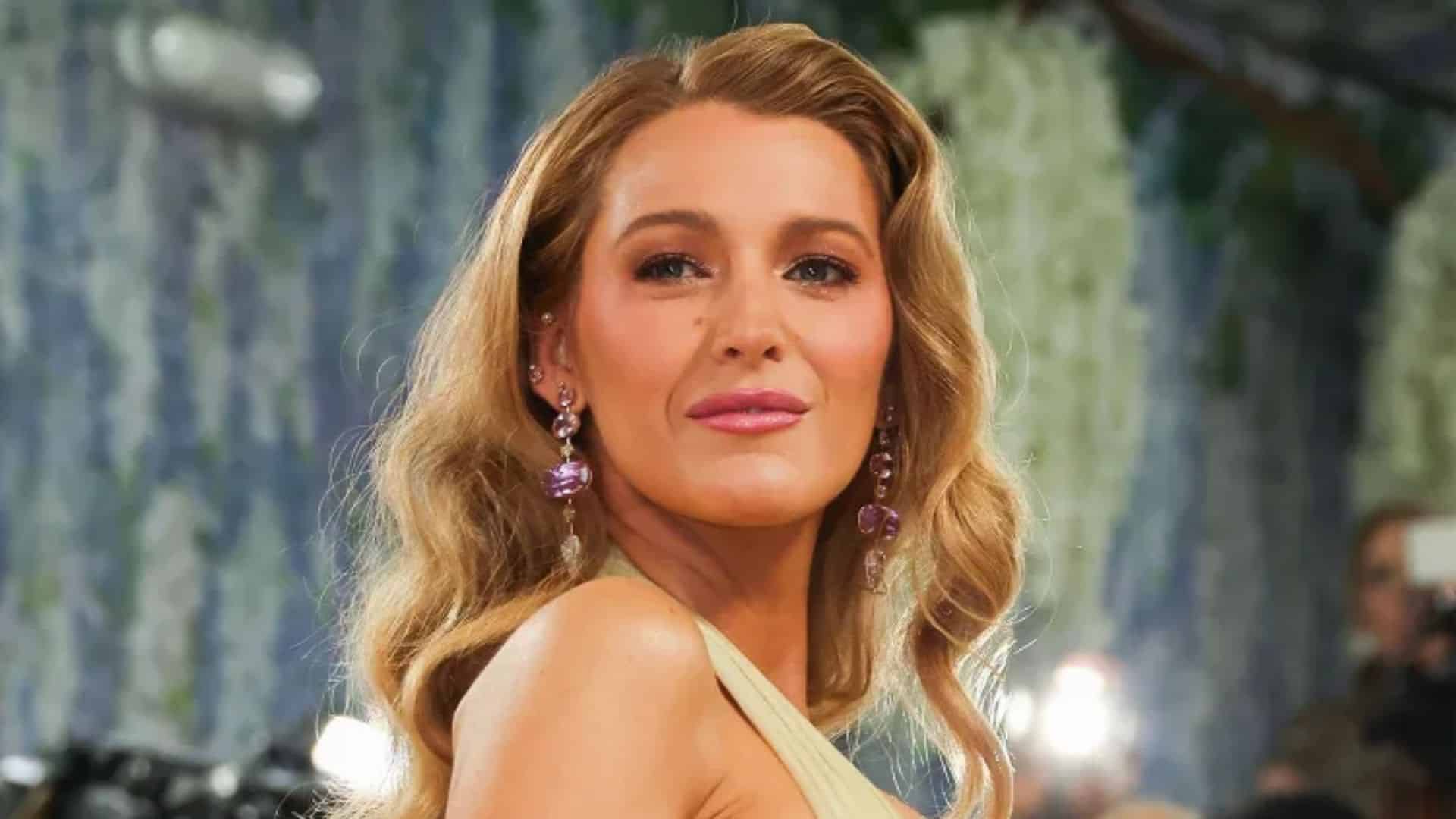 Blake Lively posing on the red carpet with soft waves, glam makeup, and dangling earrings