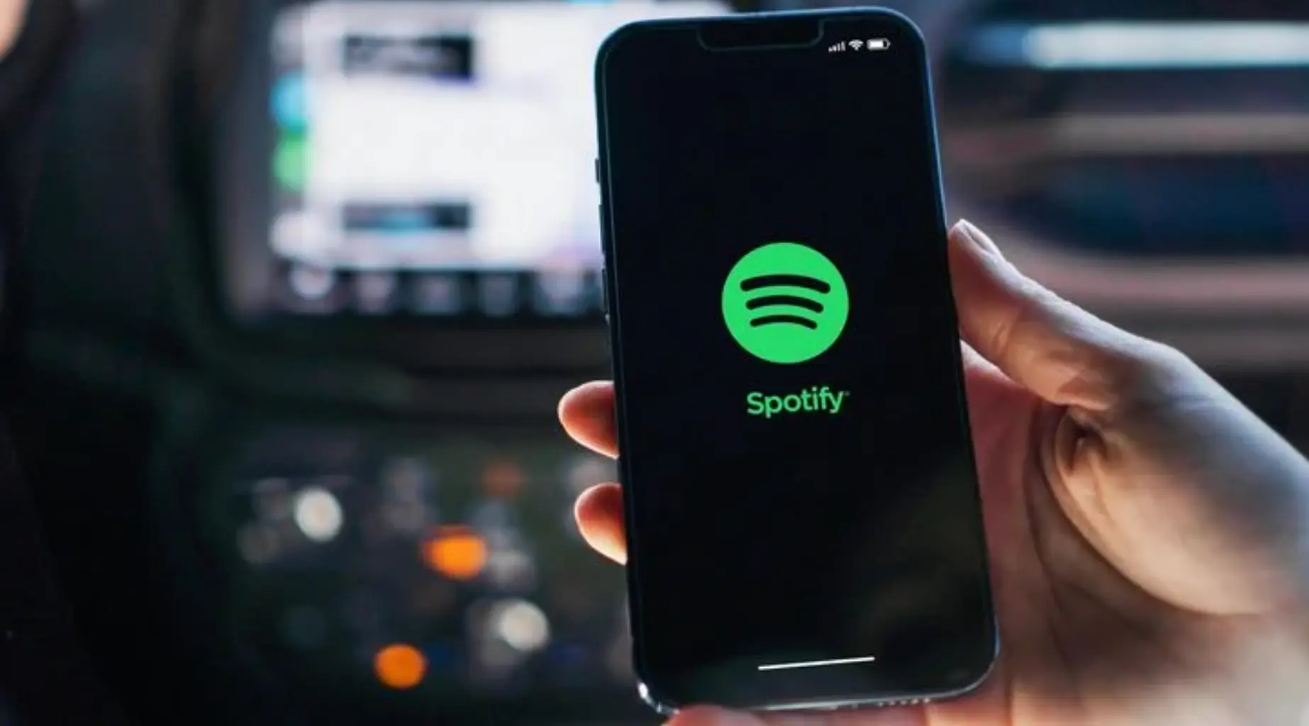Close-up of a phone displaying the Spotify app logo with a blurred background, showing the green Spotify icon on a dark screen.
