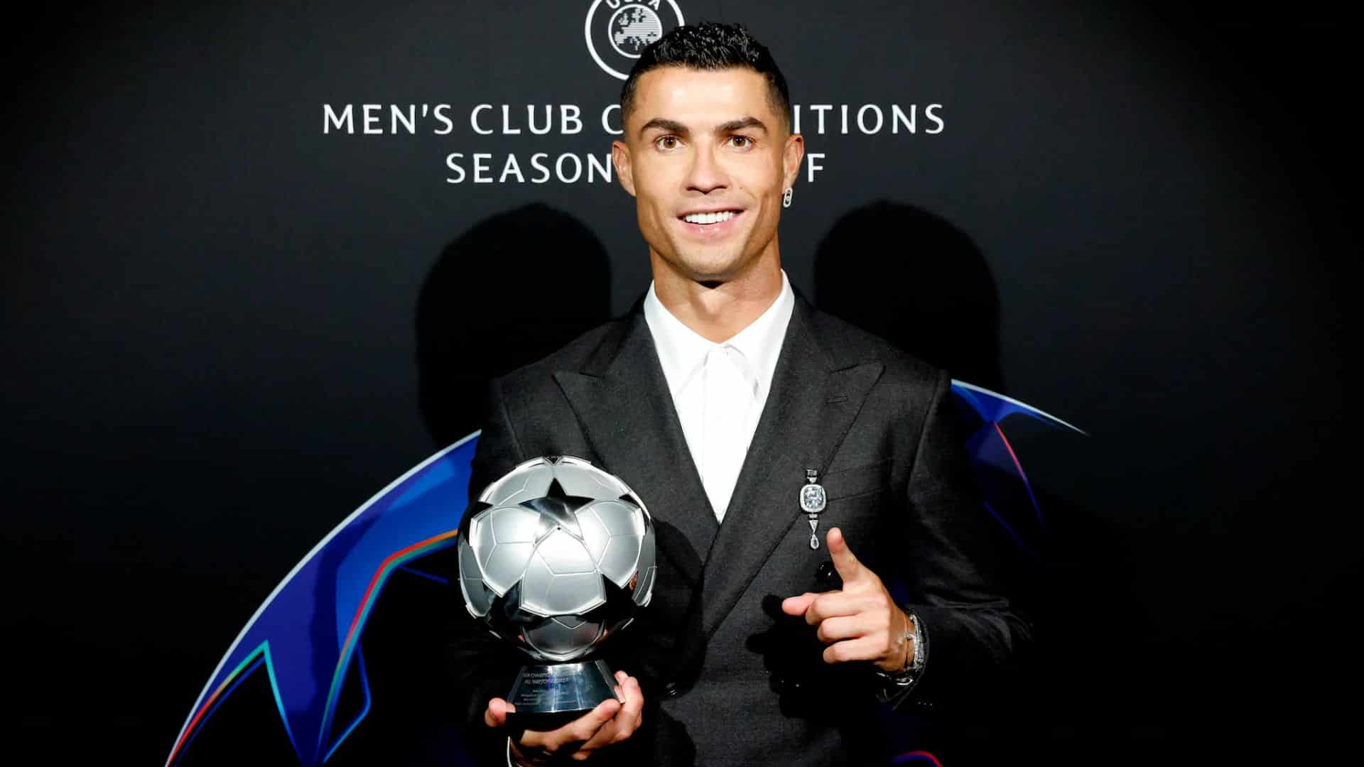 Cristiano Ronaldo in a sharp black suit proudly holding a UEFA Men's Club Competitions award trophy