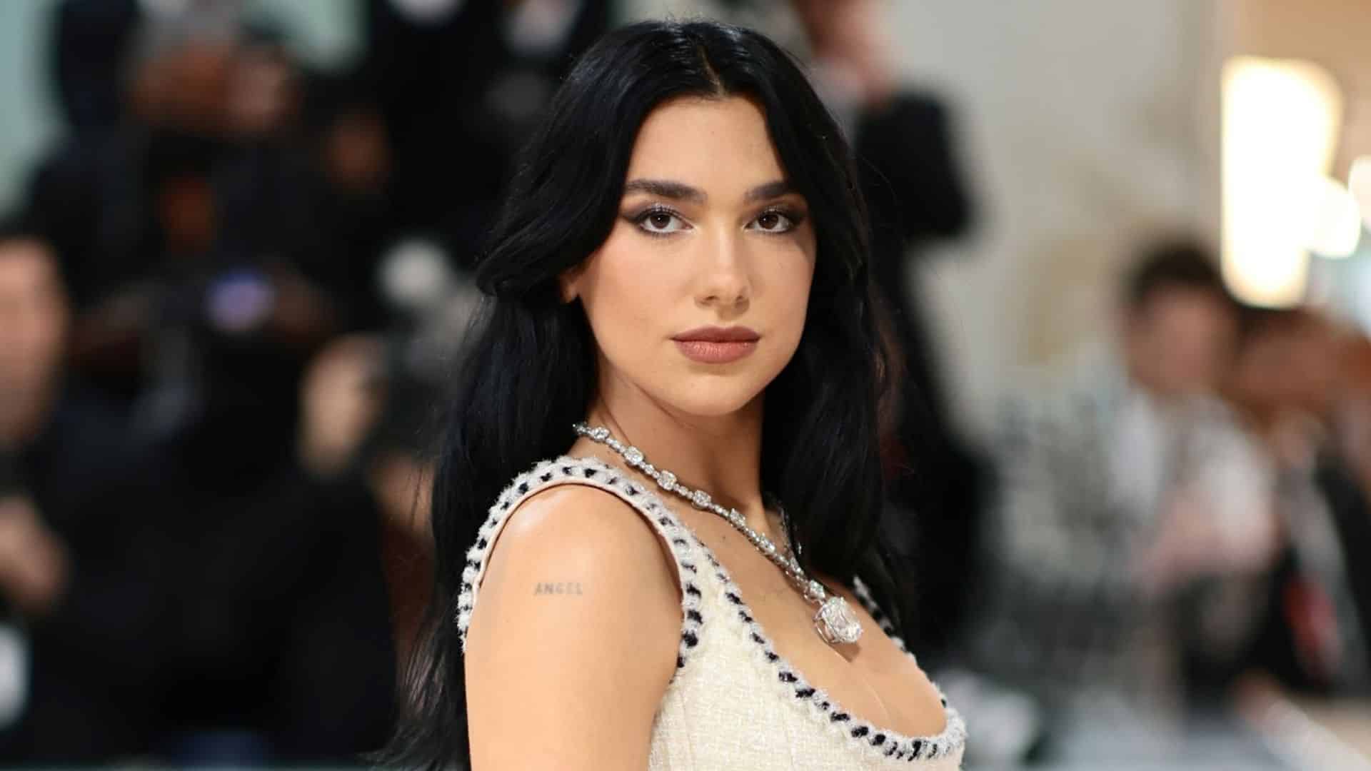 Dua Lipa posing at a red carpet event wearing a white dress and diamond necklace