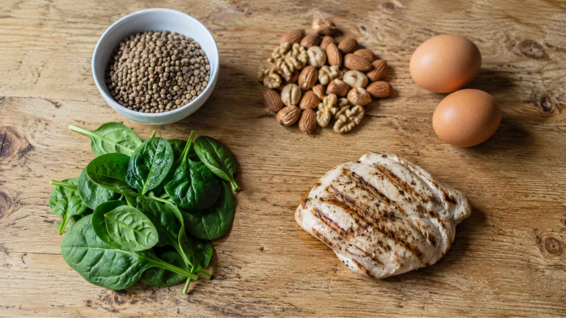 Hair-healthy foods including eggs, spinach, nuts, and lentils on a wooden table