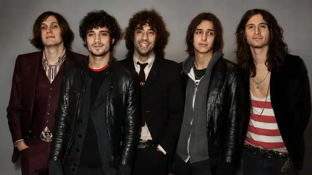 Five members of The Strokes posing together in a studio portrait with casual and edgy outfits