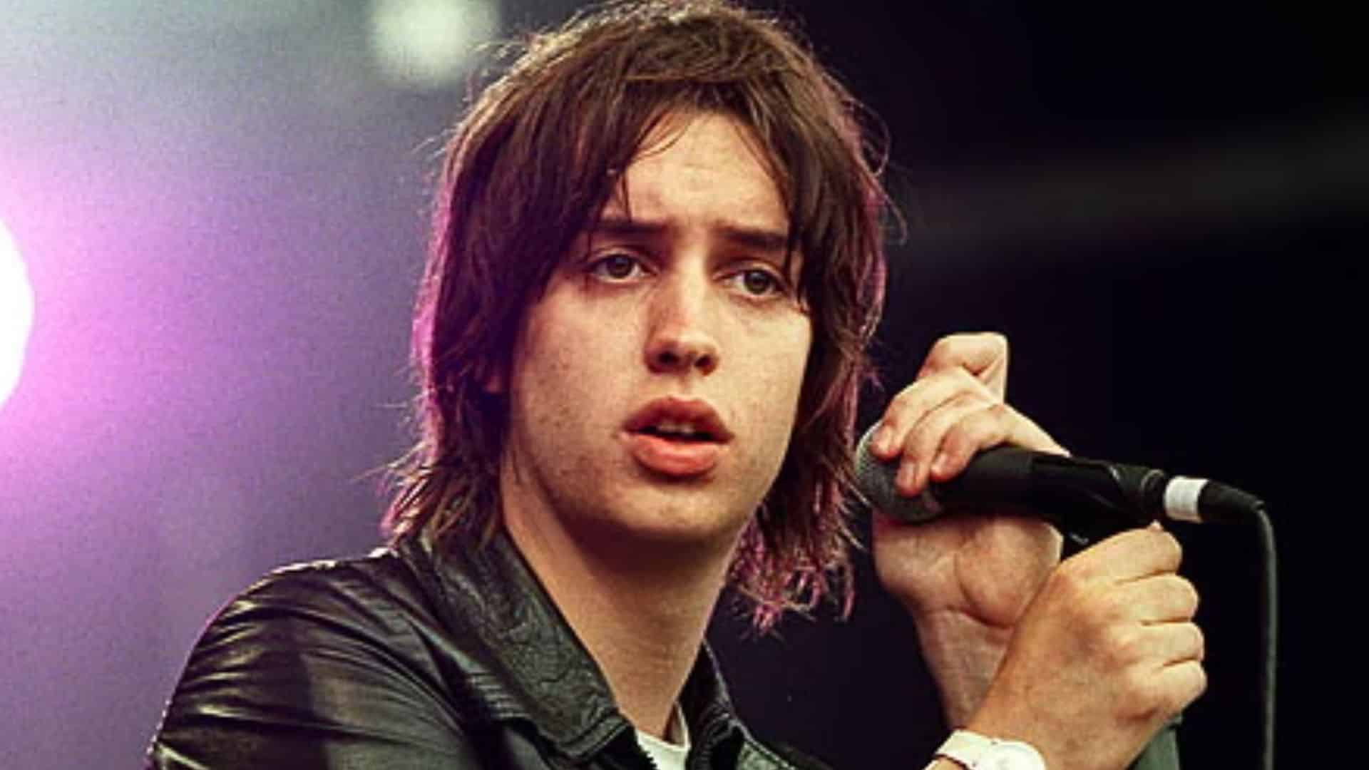Julian Casablancas, lead singer of The Strokes, performing on stage with his signature leather jacket and intense presence