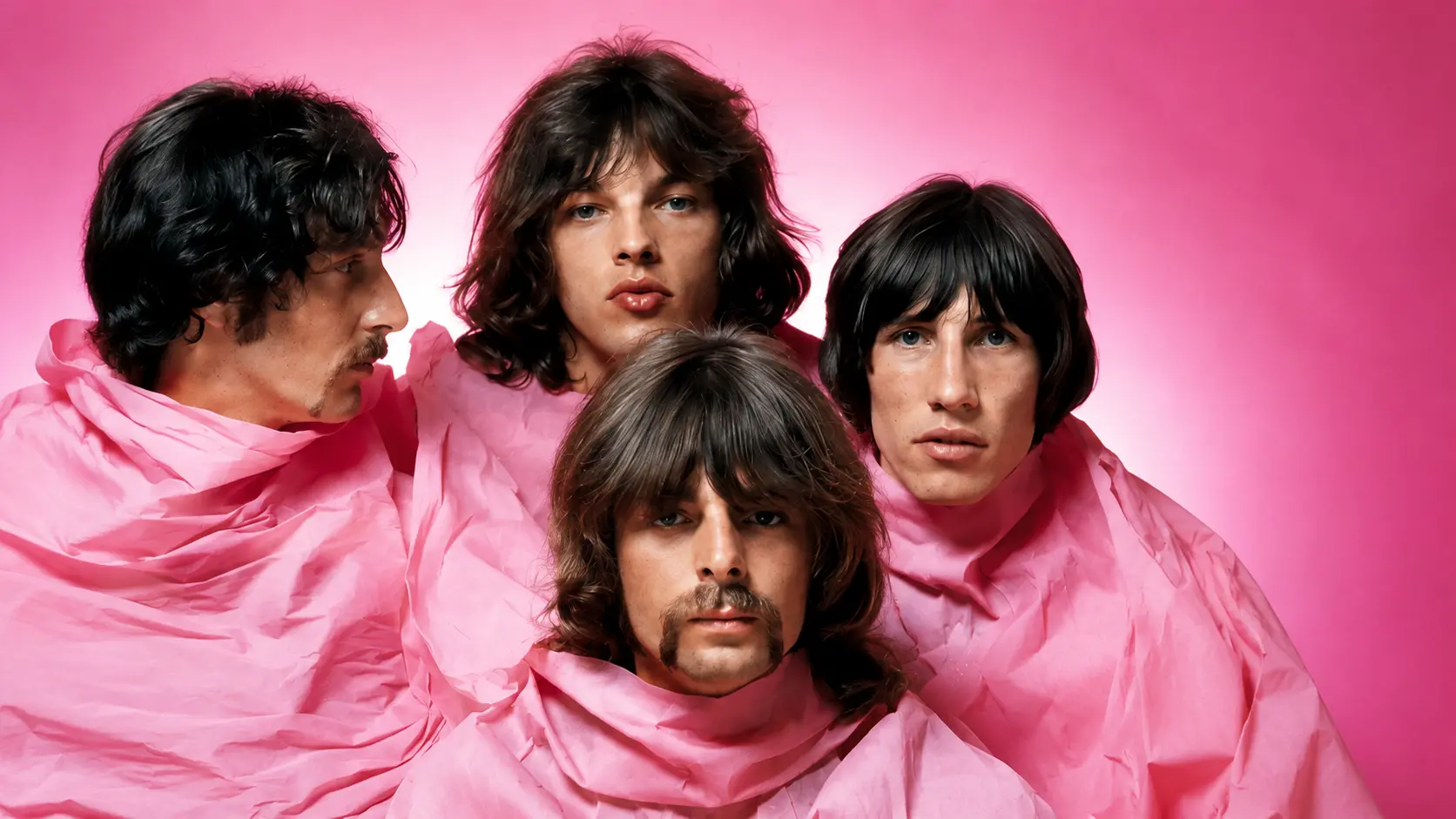 Studio portrait of Pink Floyd band members wrapped in pink fabric against a pink backdrop