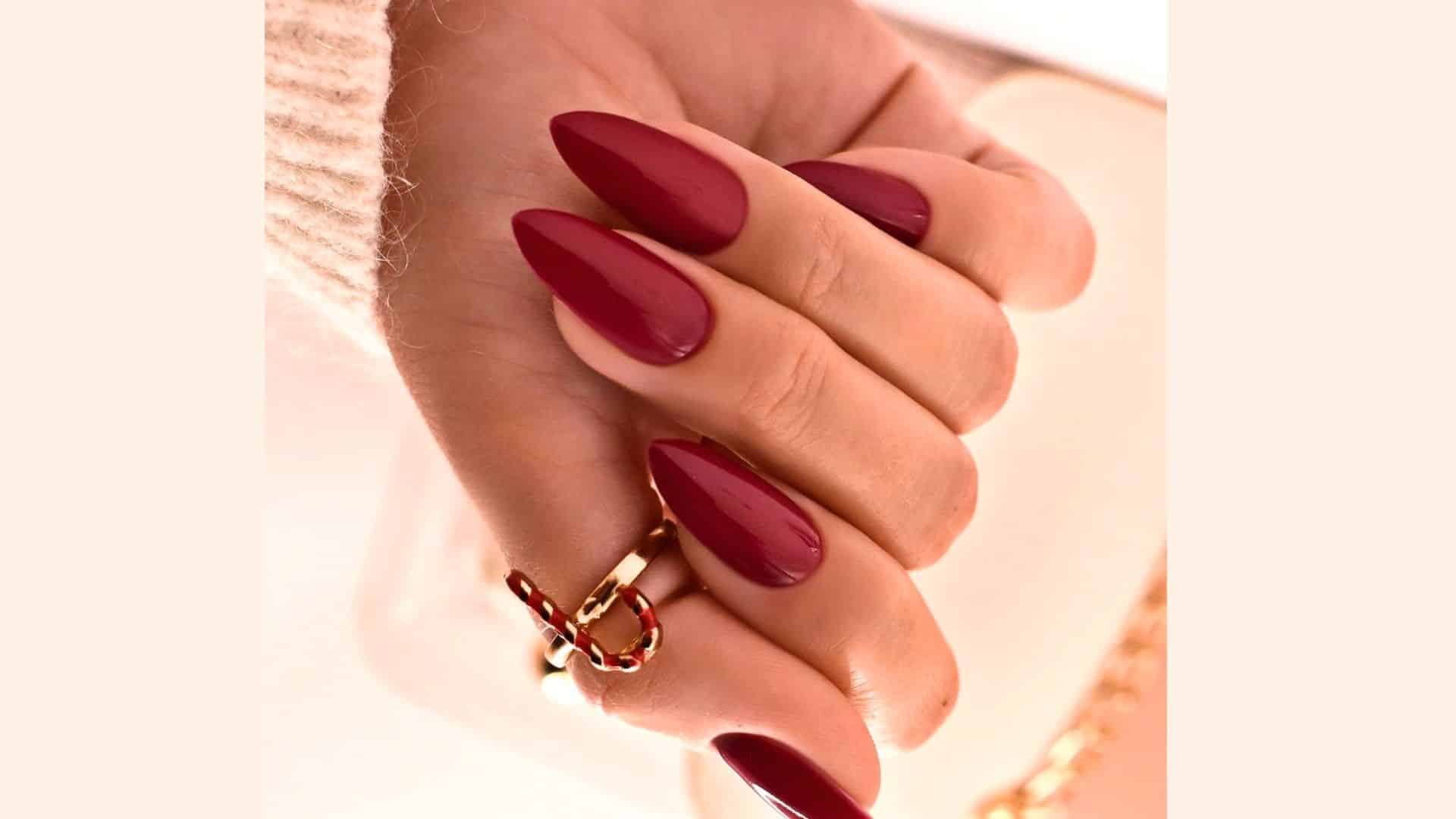 A hand with Dark Burgundy Nails, featuring a glossy finish and accented with a gold ring