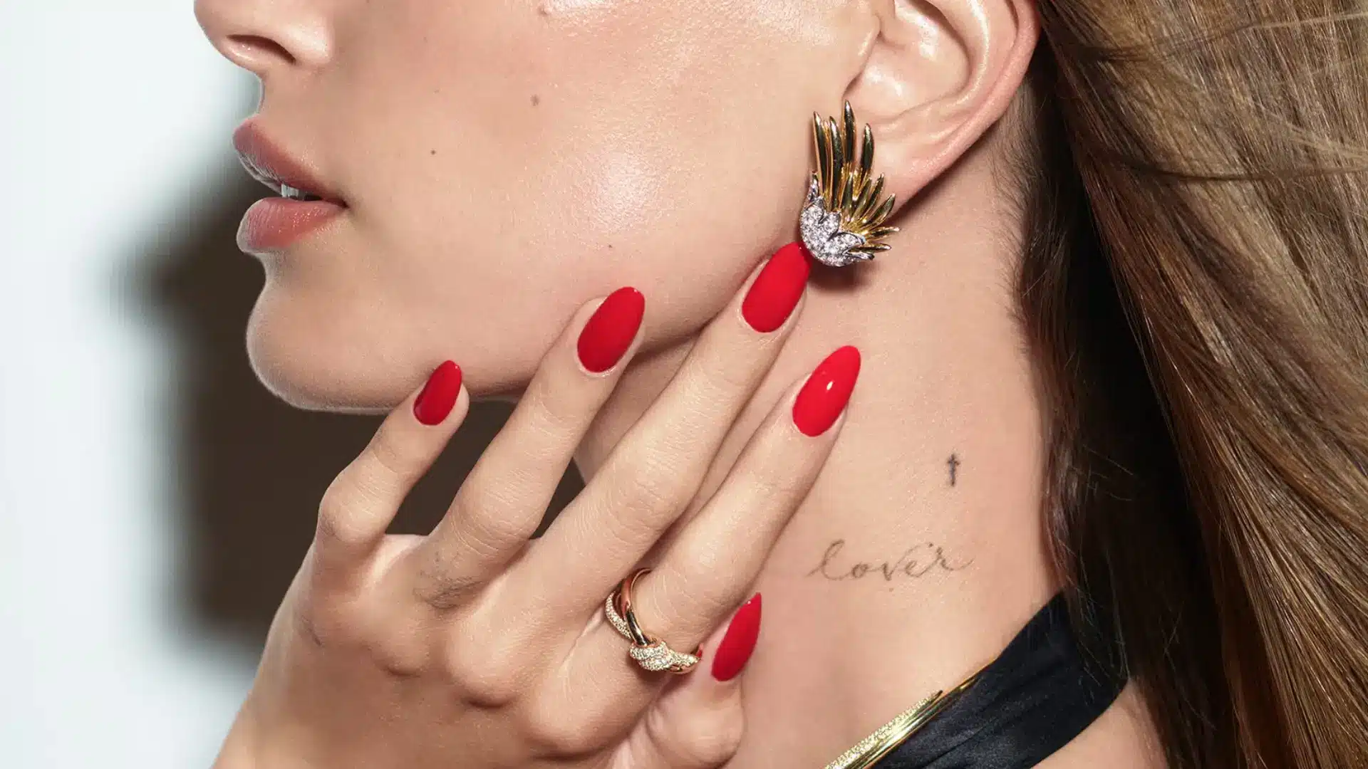 A person showing off Bold Red Nails with statement jewelry and a visible tattoo
