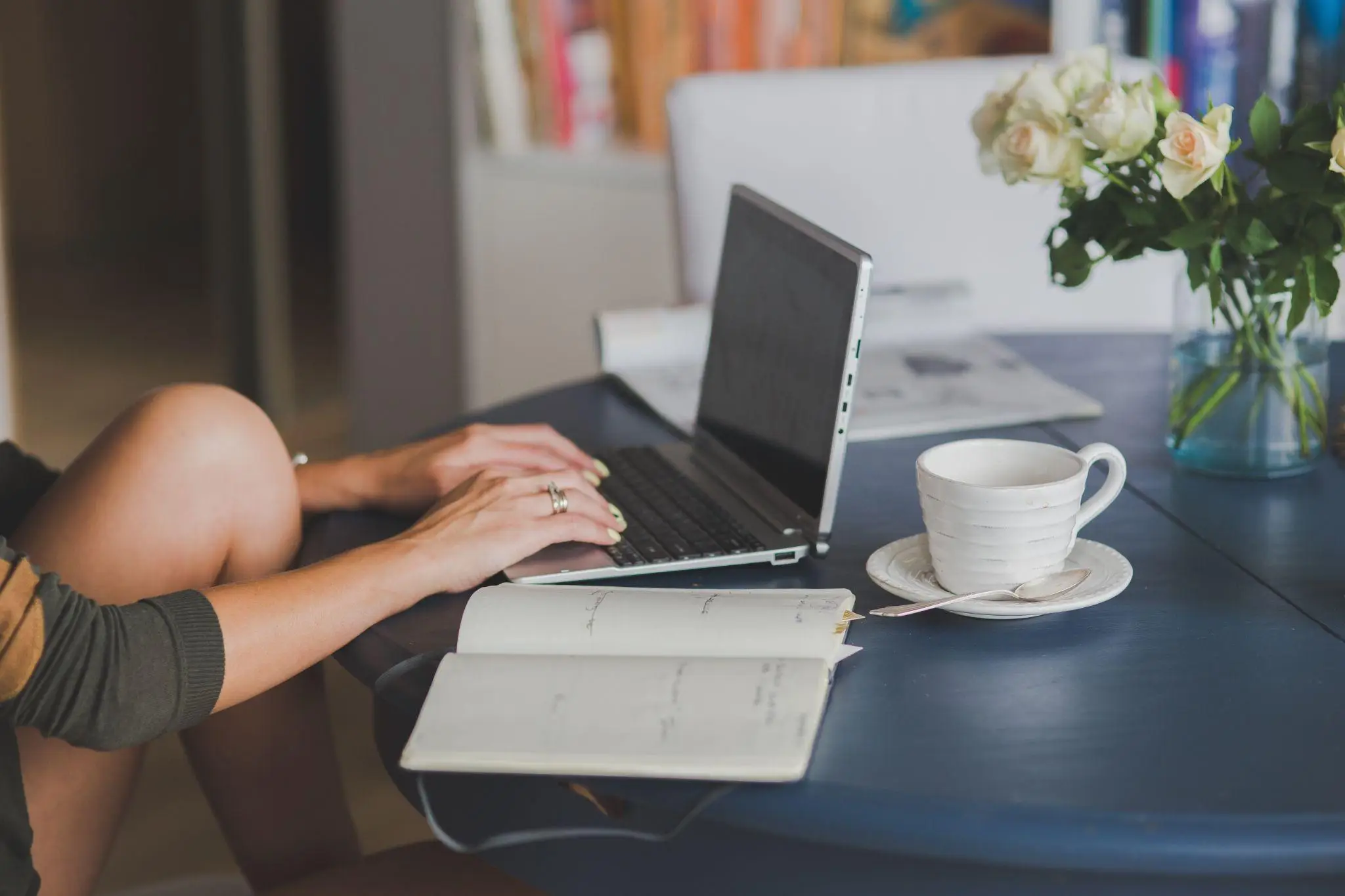 Hands typing on laptop at round table with notebook and coffee cup