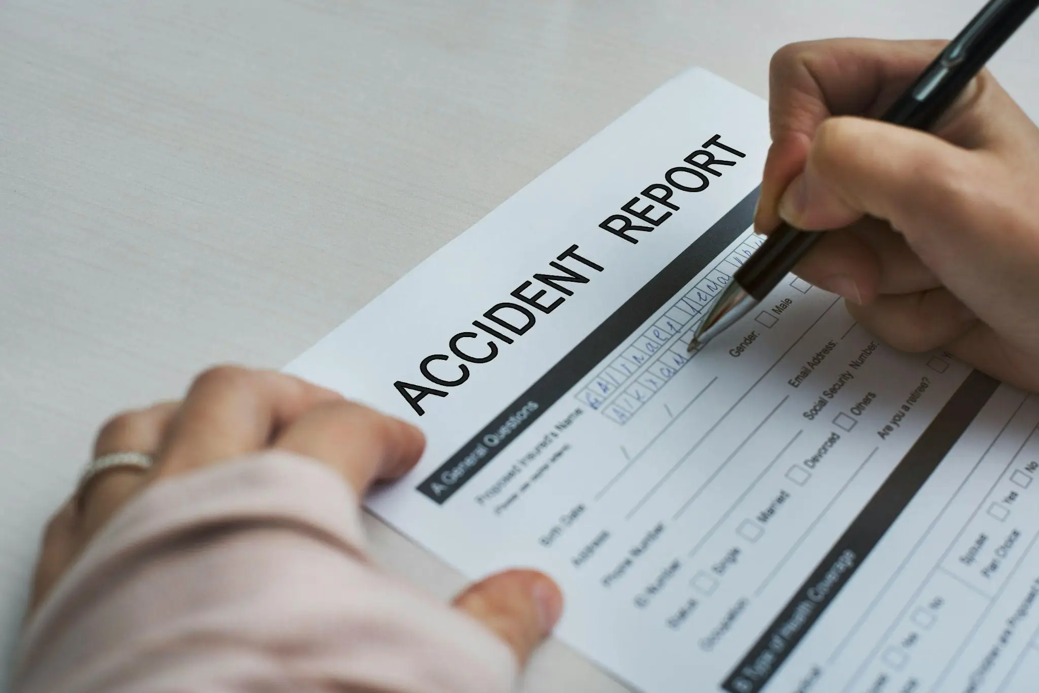Person filling out accident report form with a pen on a light-colored desk