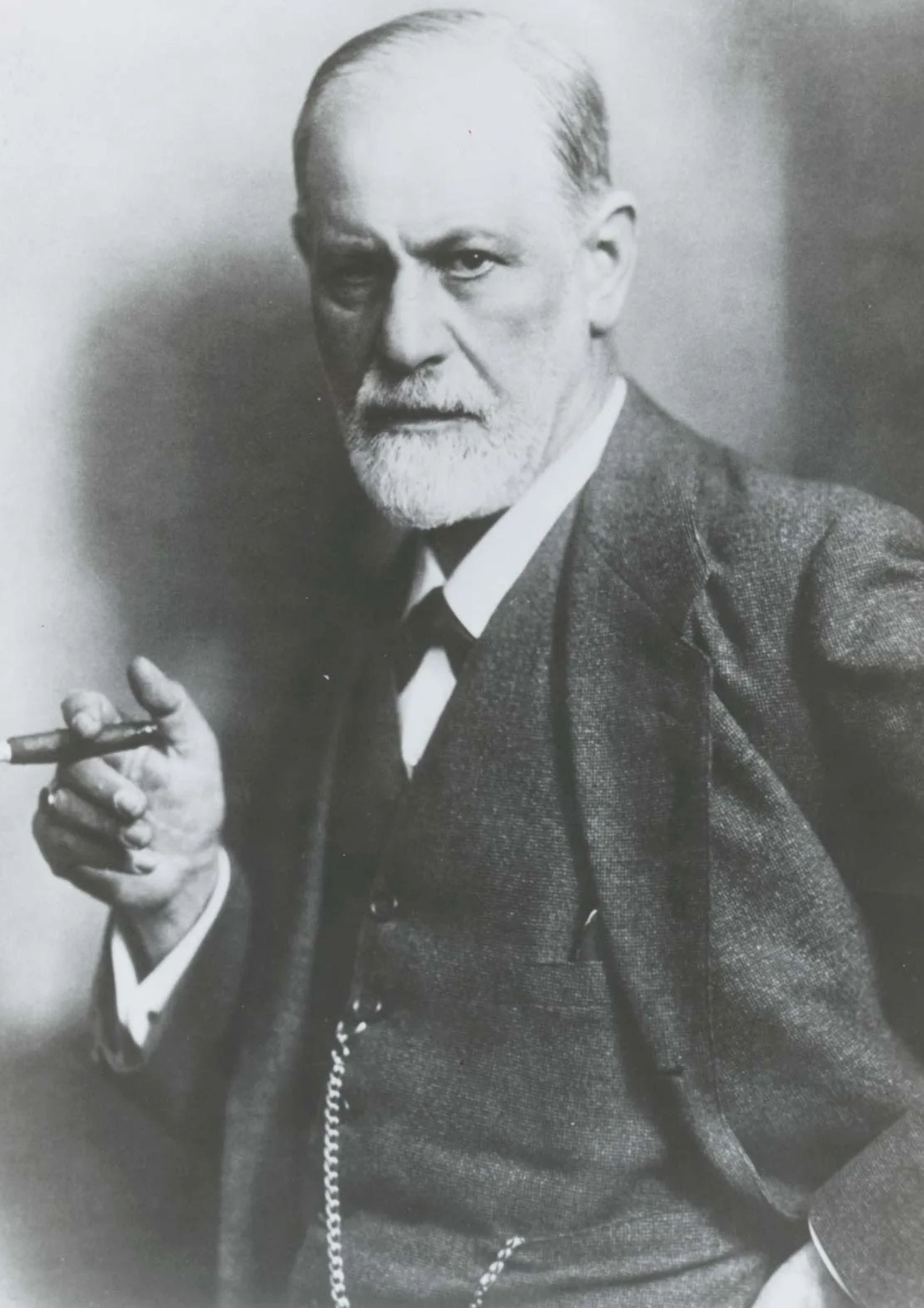 Black and white portrait of Sigmund Freud holding a cigar, wearing a suit and staring toward the camera (1)