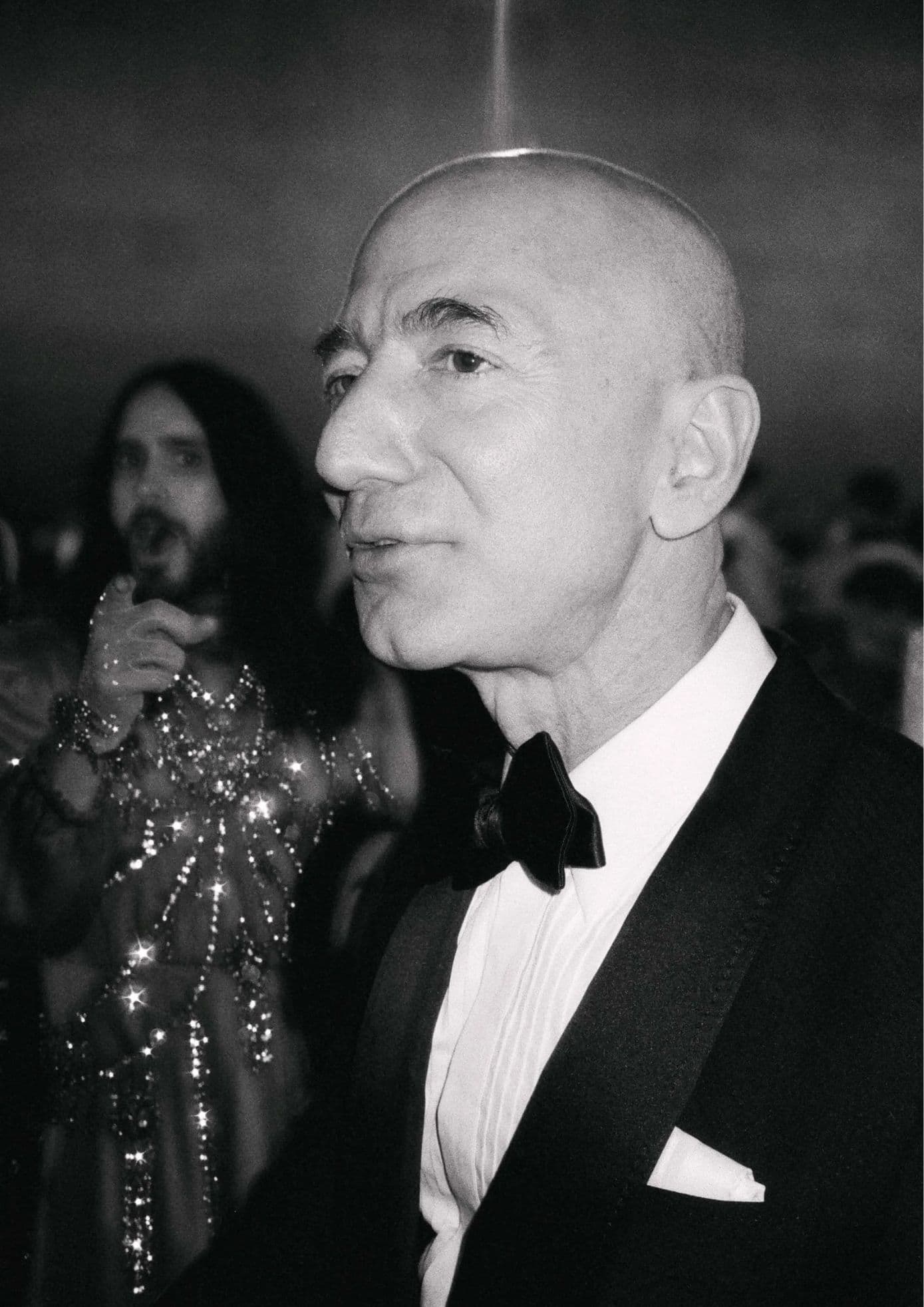 Black-and-white shot of Jeff Bezos in a tuxedo at the 2019 Met Gala, with Jared Leto in the background. (1)