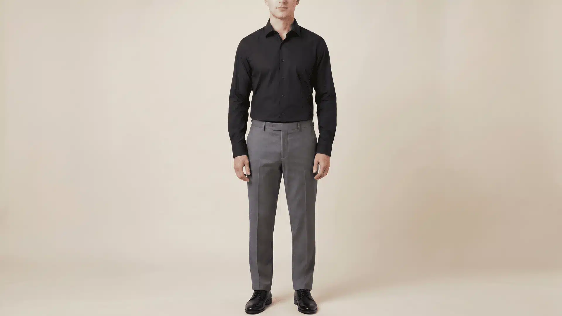Man wearing a black long-sleeve shirt with charcoal grey pants and black shoes, standing in a neutral background.