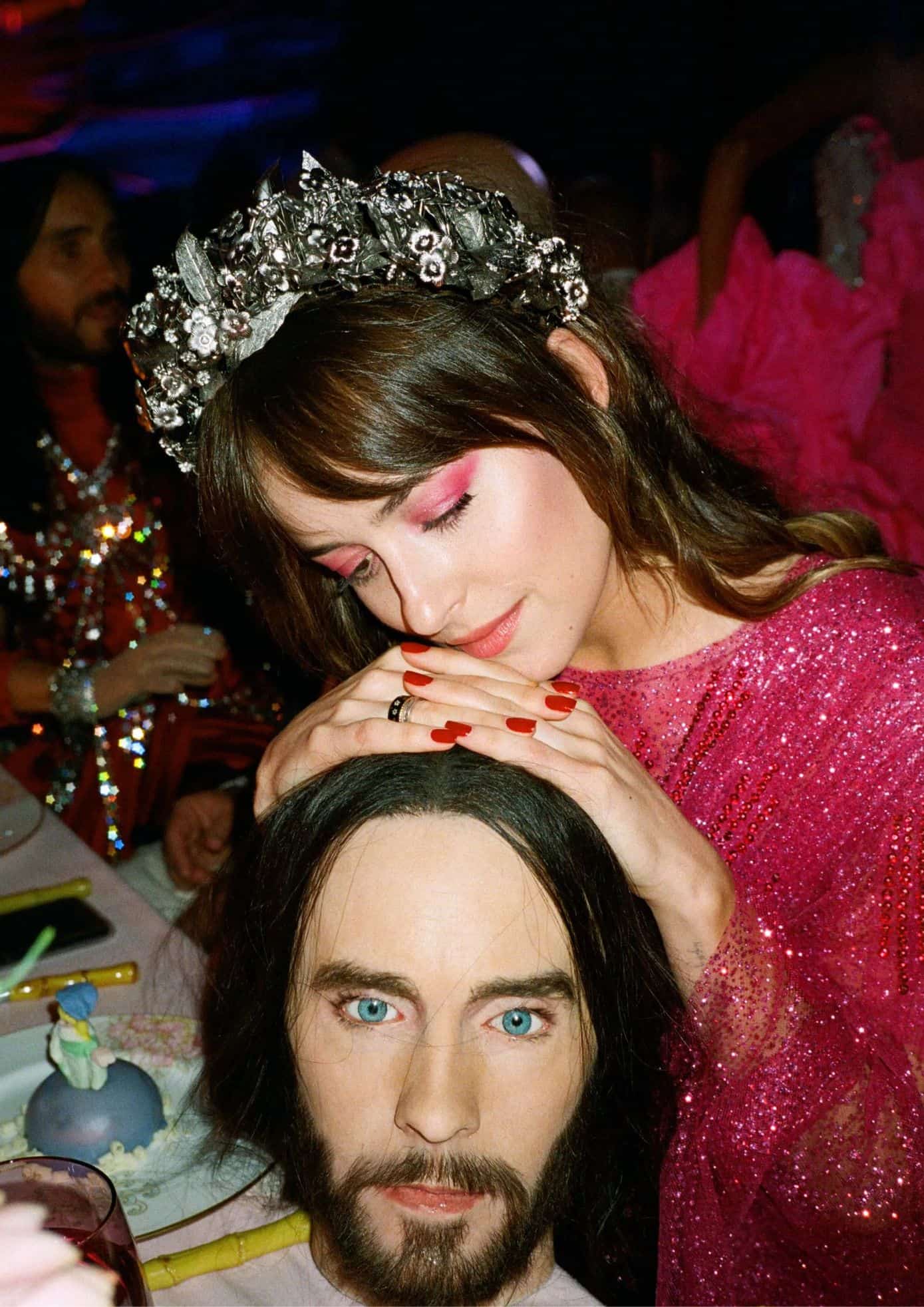 Dakota Johnson in a pink glittering gown with a floral crown, resting her hands on a mannequin head at the event. (1)