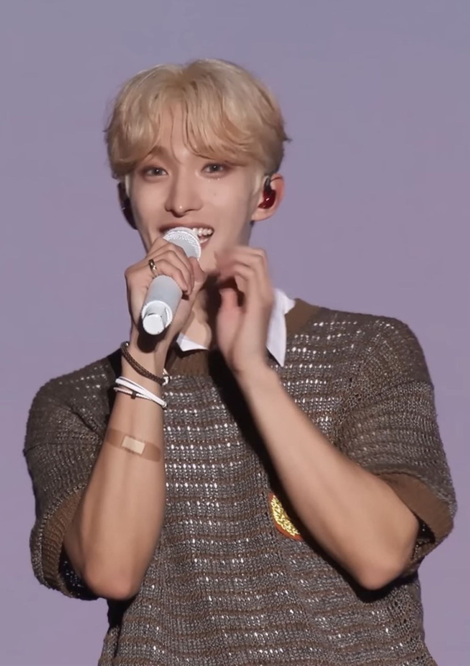 DK of Seventeen singing on stage, wearing brown sweater, holding white microphone, smiling during performance.