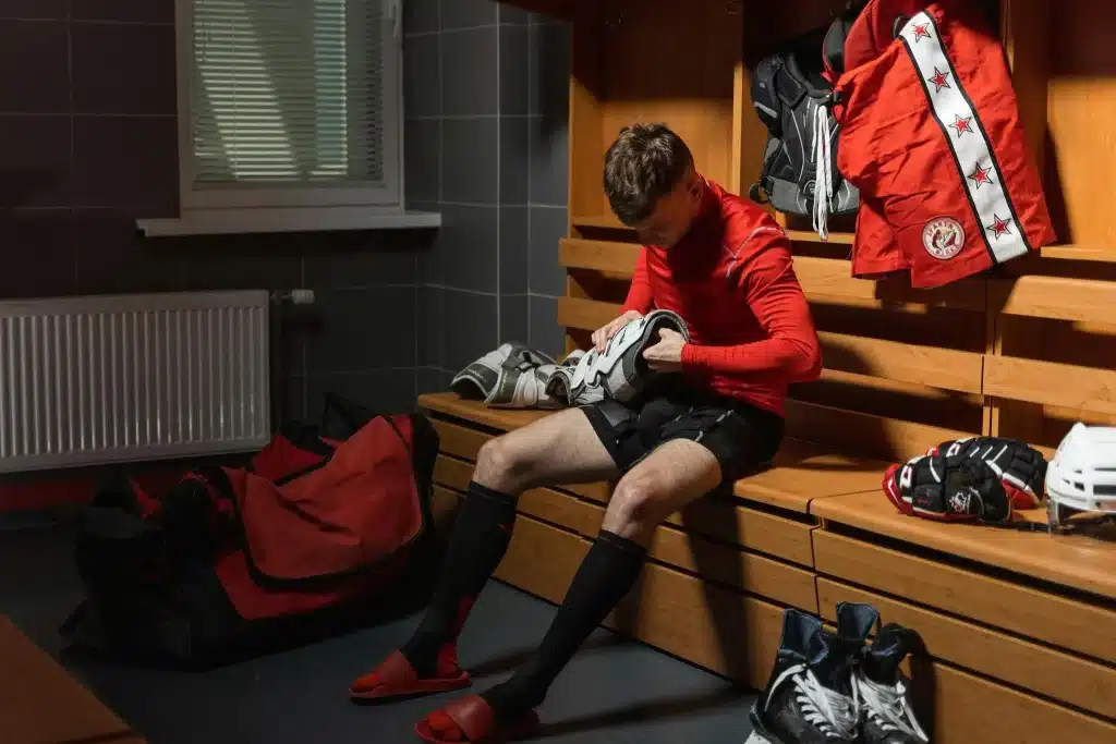 Hockey player in red jersey preparing gear on wooden locker room bench