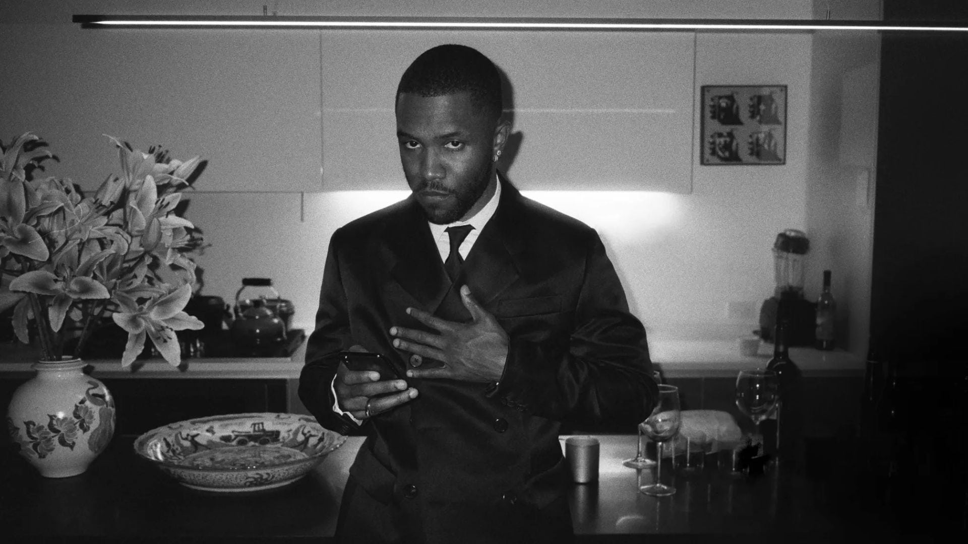 Frank Ocean in a suit at the 2019 Met Gala, standing in a kitchen and holding a phone, captured in black-and-white. (1)