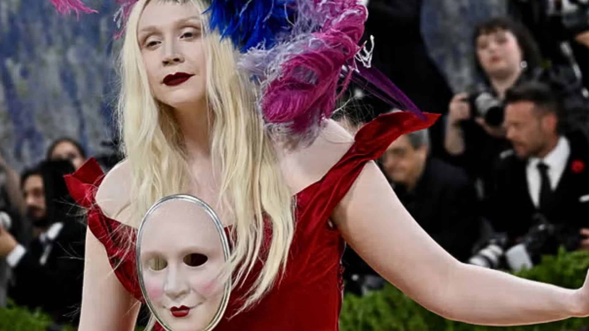 Gwendoline Christie wearing a theatrical red Maison Margiela gown with dramatic feathered headpiece and mask accessory