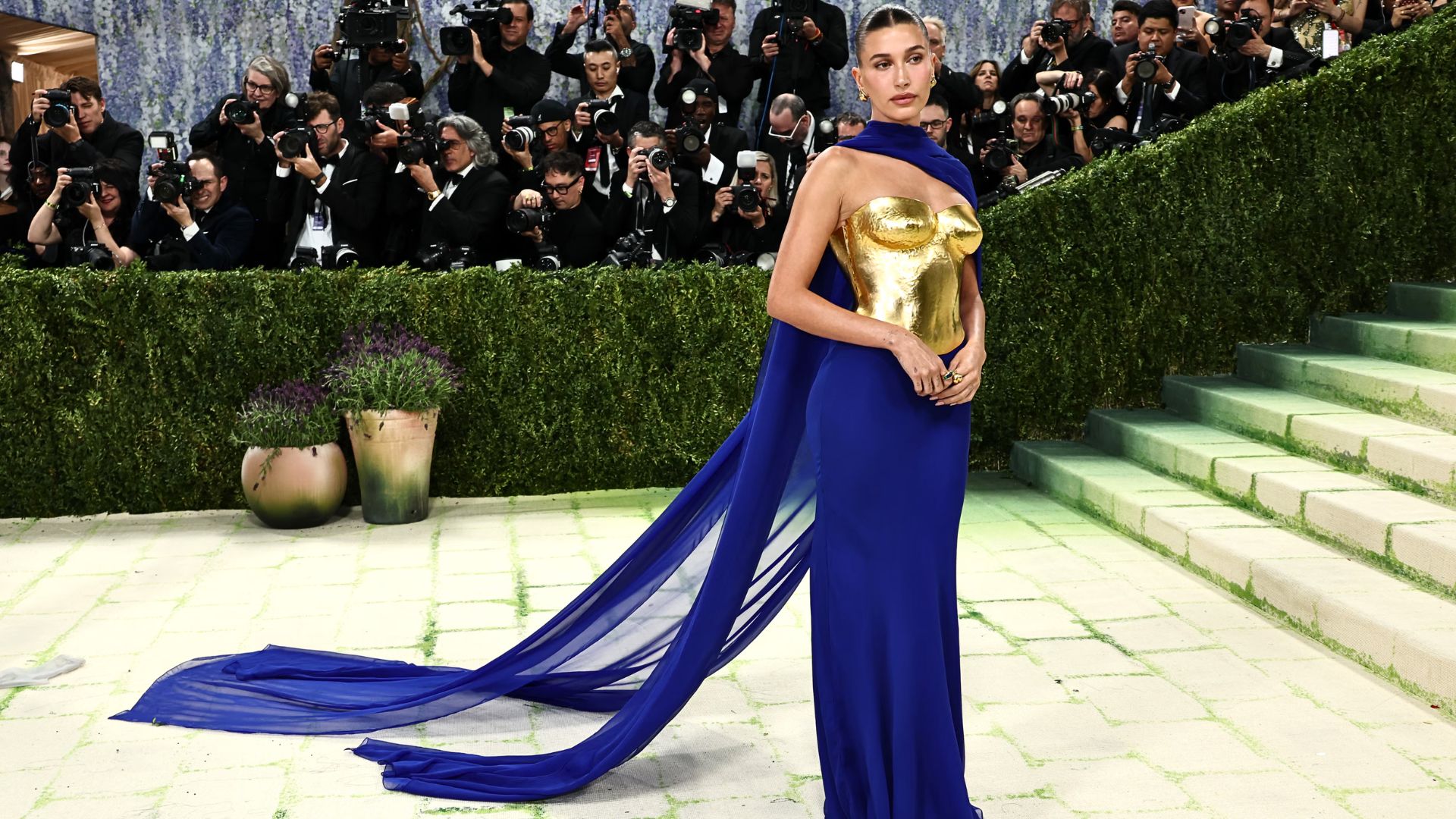 Hailey Bieber wearing a royal blue Saint Laurent gown with gold sculpted bodice and flowing cape