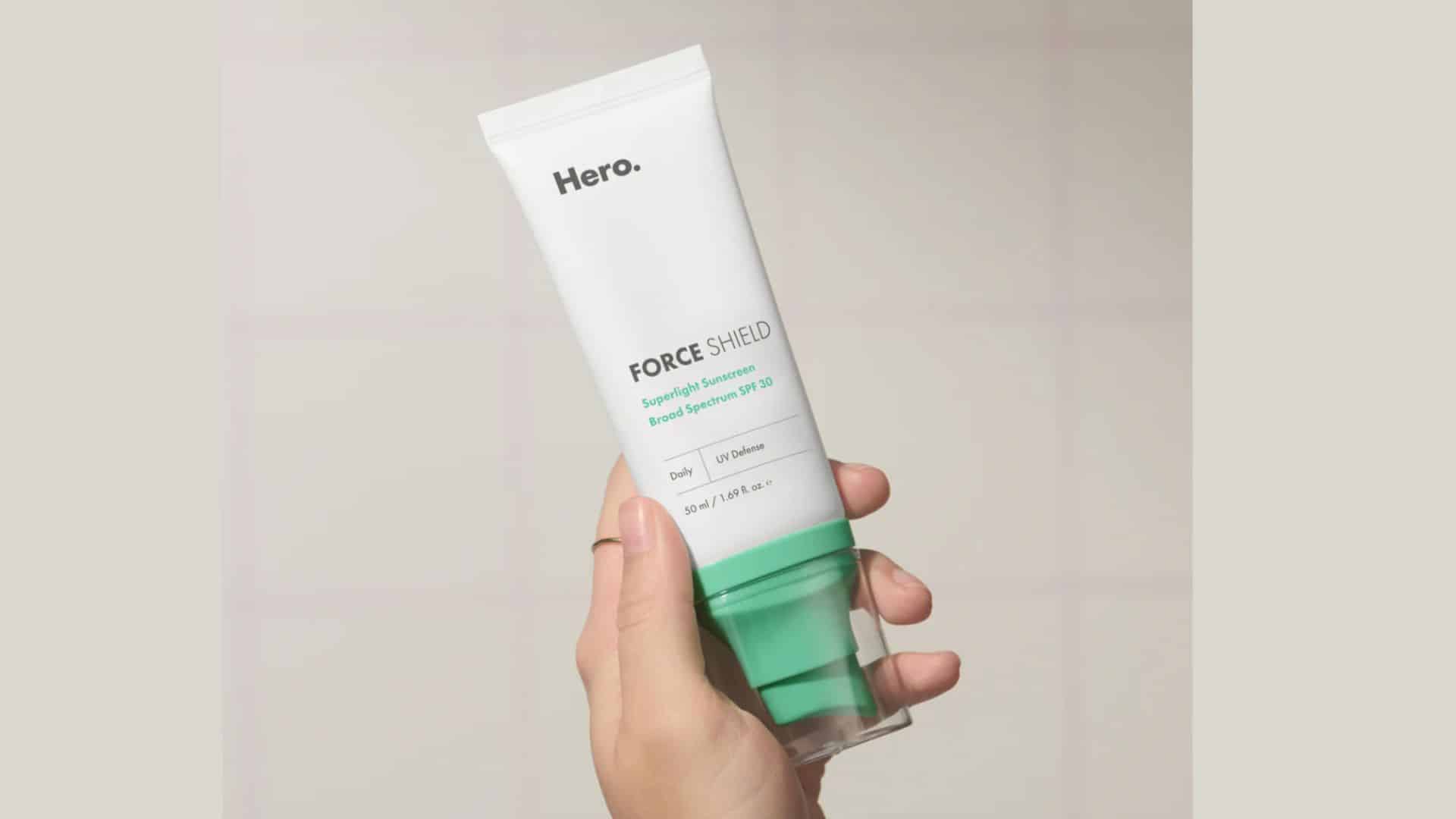 Hand holding a tube of Hero Force Shield SPF 30 superlight sunscreen with green pump