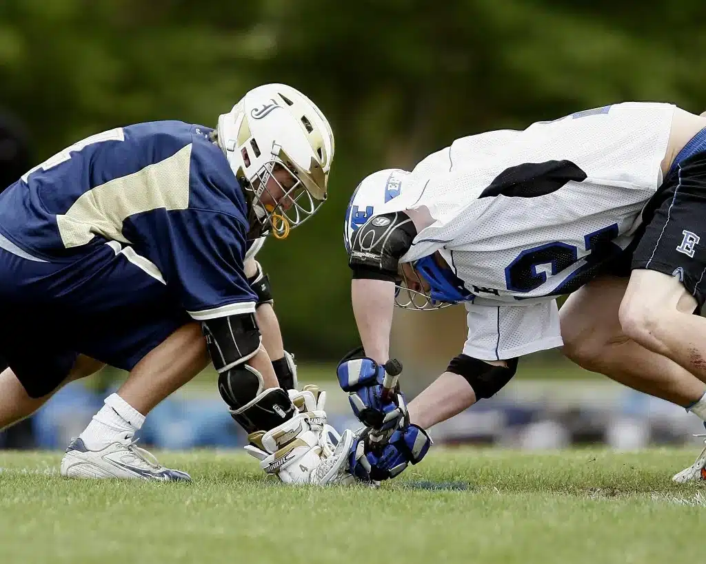 Two lacrosse players in helmets competing for the ball on grassy field