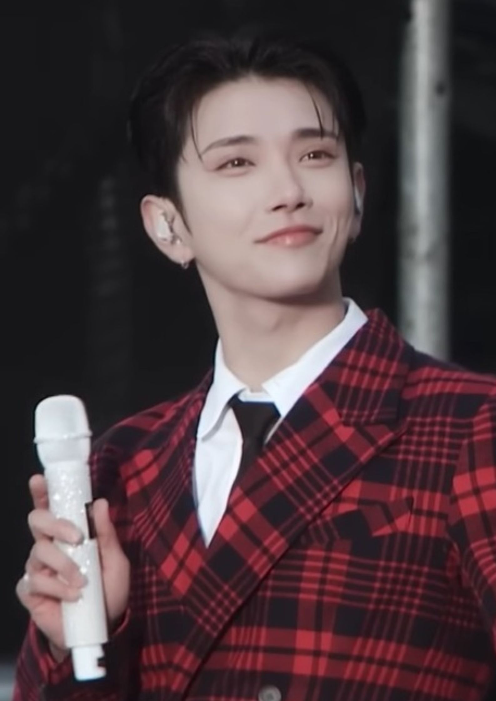 Joshua Hong of Seventeen wearing a red plaid suit holding a microphone with a calm, confident stage presence.