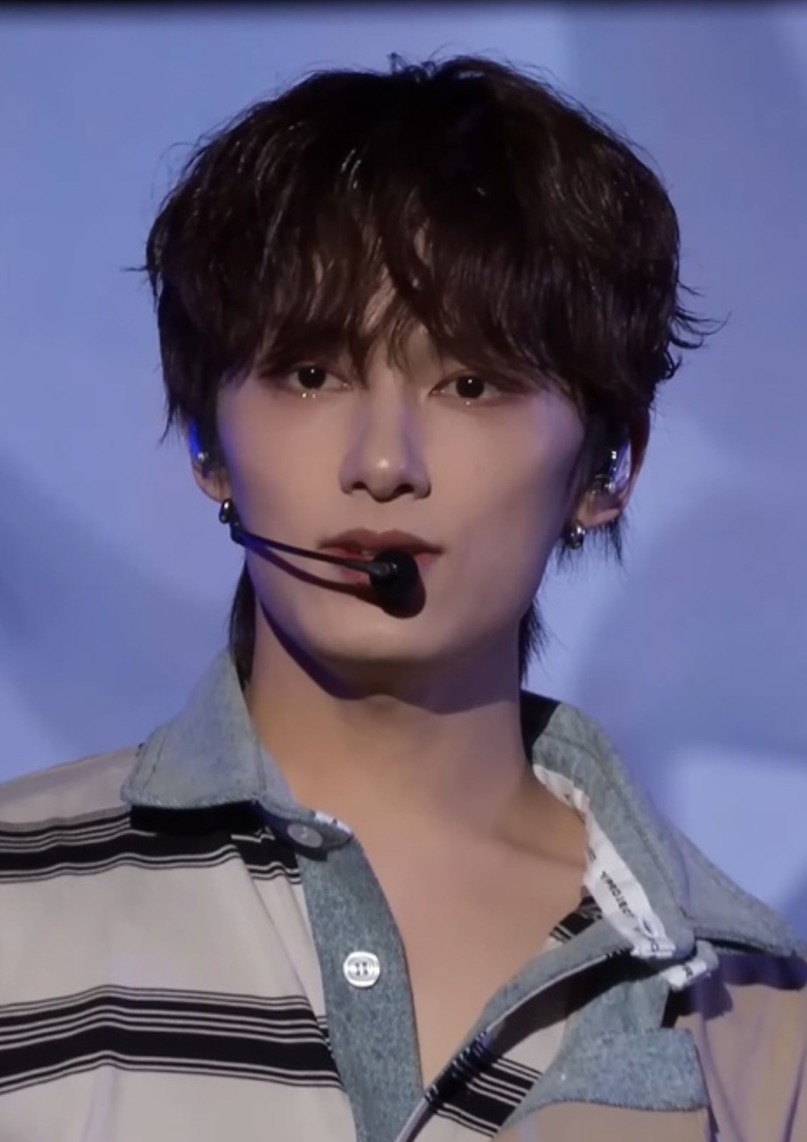 Jun from Seventeen performing on stage, wearing a striped shirt and headset microphone, looking focused.
