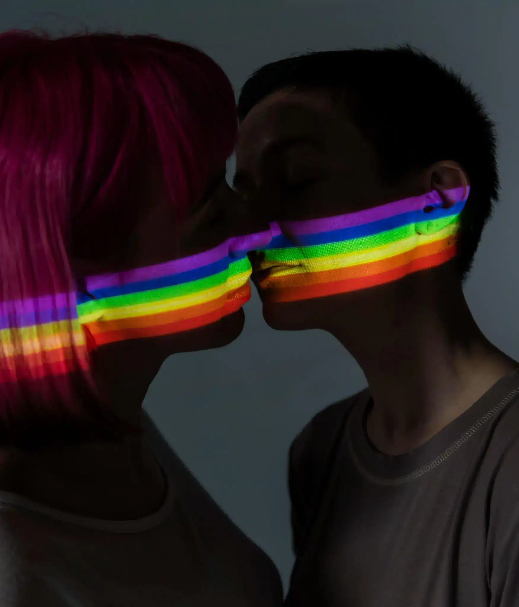 Two people kissing with rainbow light projection on faces in a dark setting