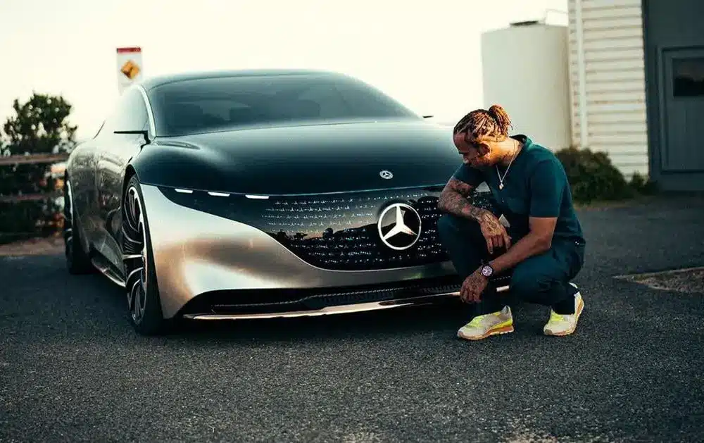 Lewis Hamilton crouching beside a futuristic Mercedes electric concept car on a quiet road