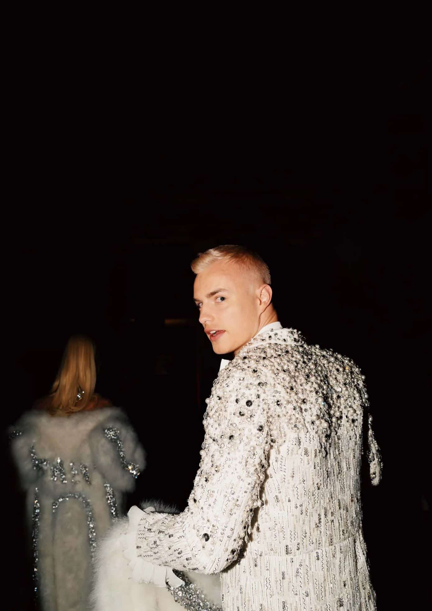 Man in a sequined white suit with sparkling embellishments and a fur-lined coat. (1)